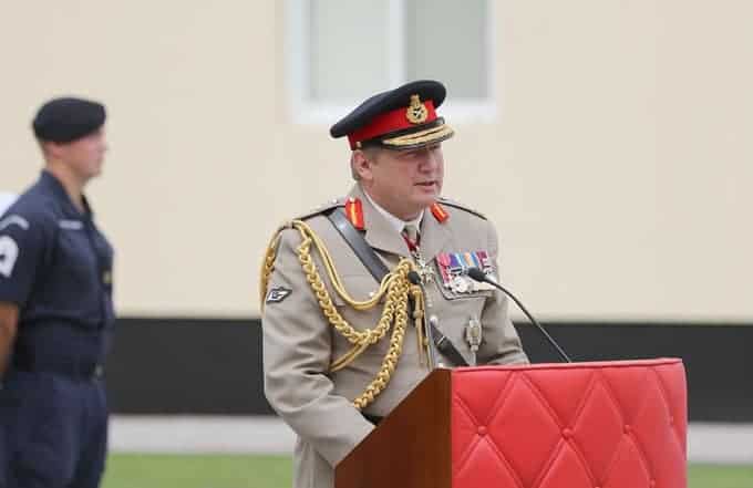 Sir Chris Deverell, the founder of Deverell Innovation Ventures, standing in service dress at a lectern addressing an audience. Standing behind Sir Chris Deverell is another service-man.